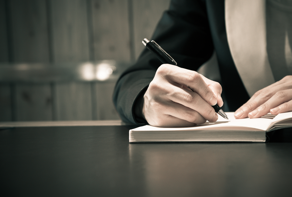 Mão redigindo sobre caderno — análise de contrato de trabalho