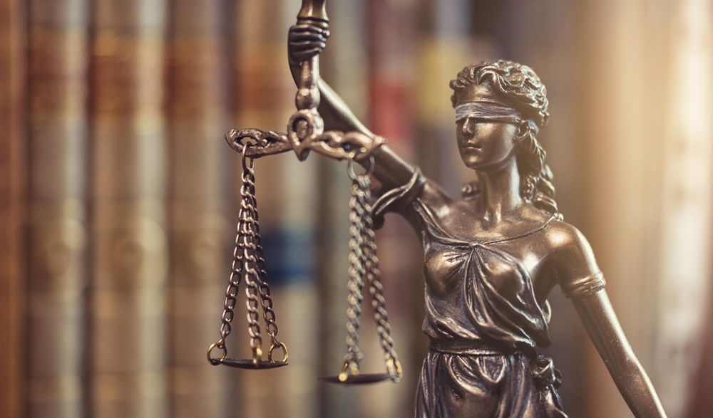 Estátua da Justiça com livros de lei, simbolizando a complexa defesa técnica no Tribunal do Júri para o crime de Infanticídio.